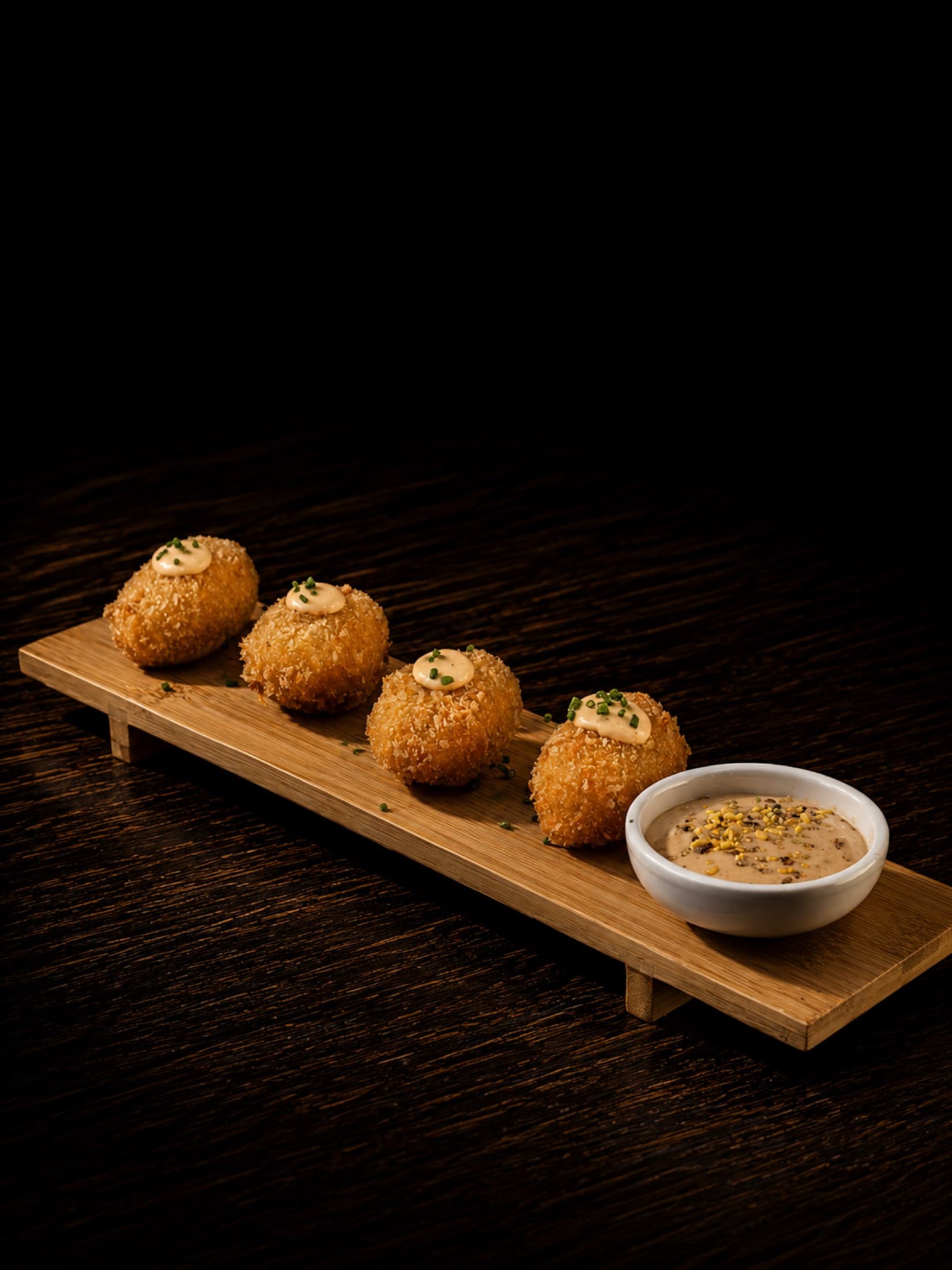 Croquetas caseras sobre tabla oscura, con su salsa para mojar
